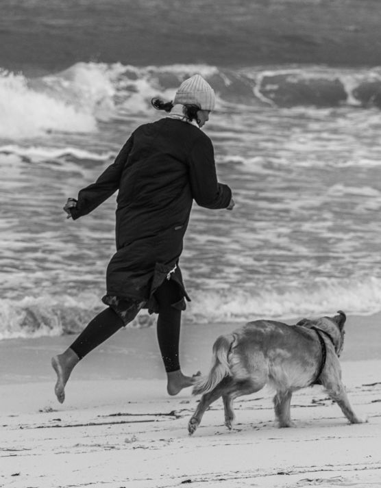 a person running on a beach with a dog